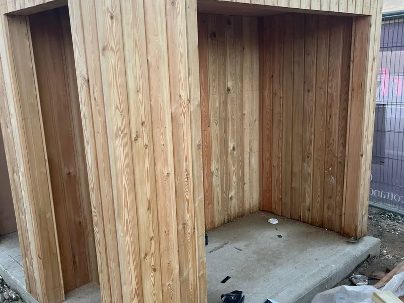 Timber clad store with two open bays lined with vertical boards on a concrete base