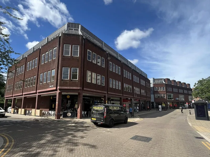 Sign written van parked outside a three storey brick town centre building with shops below