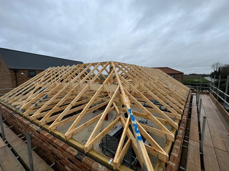 Newly erected timber trusses forming a hipped roof on brick walls seen from scaffolding