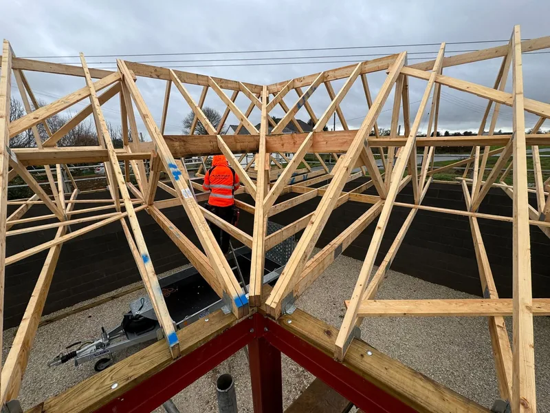 Carpenter in hi vis working among newly erected timber roof trusses