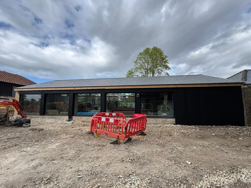 Long single storey building with black timber cladding and a dark roof on a cleared site