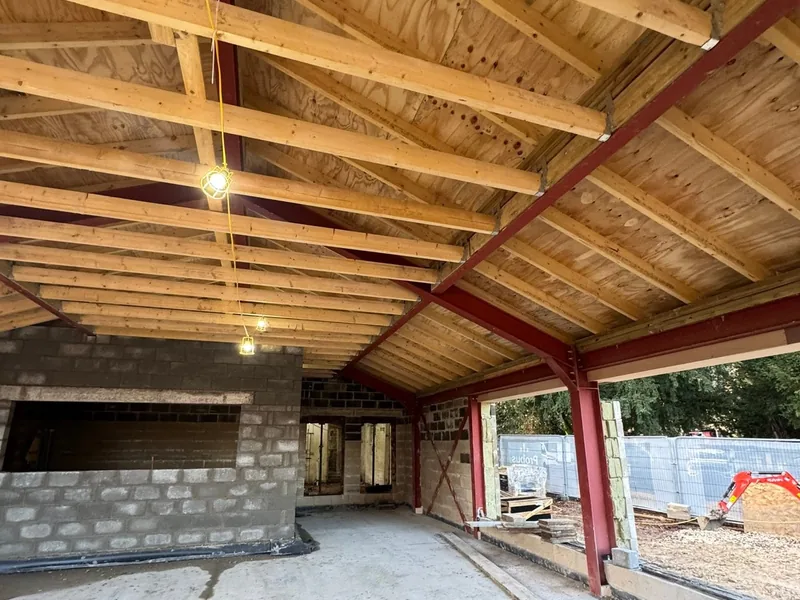 Timber roof deck and rafters on red steel beams inside a building under construction