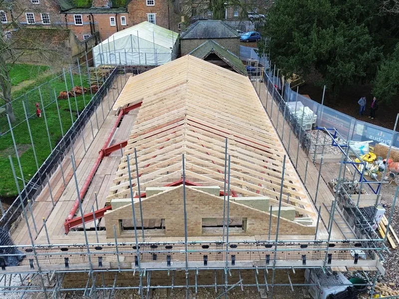 Aerial view of a new hipped timber roof structure on red steelwork with scaffolding around