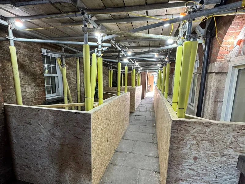 Hoarded walkway with yellow steel props supporting the ceiling inside a building