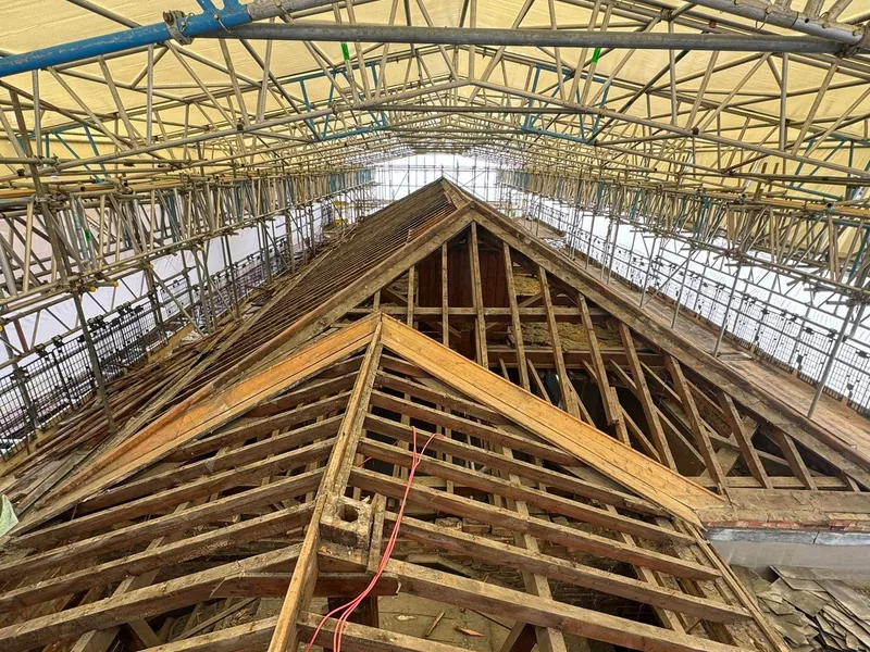 Stripped timber roof structure and gable end under a temporary scaffold roof