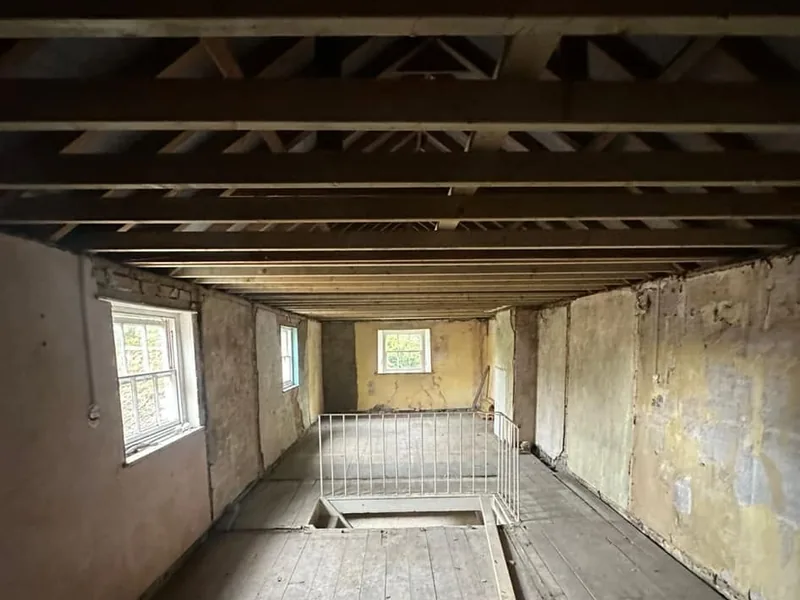 Stripped first floor with exposed roof timbers and a temporary stair barrier