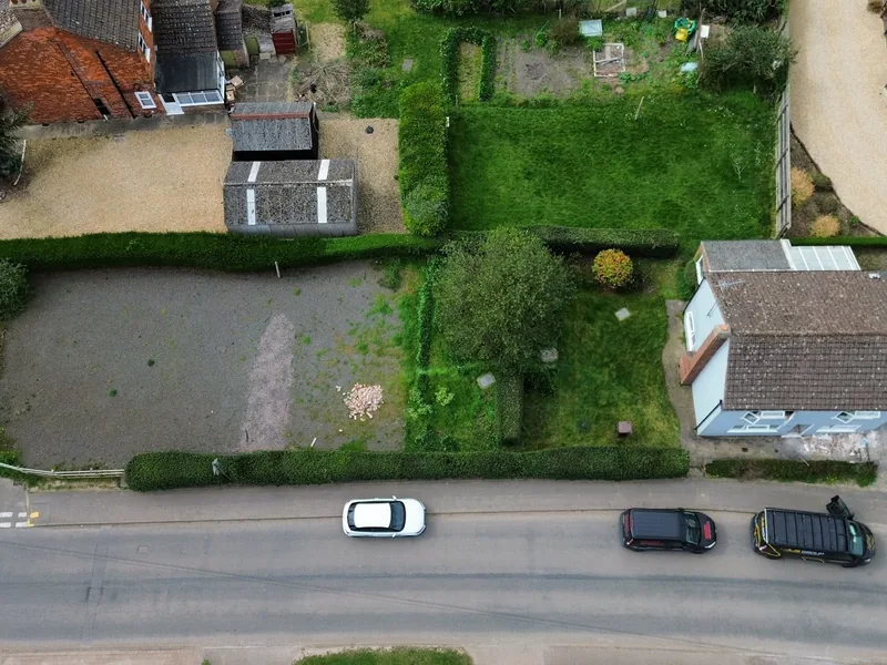Aerial view of a cleared plot with old outbuildings beside a village road