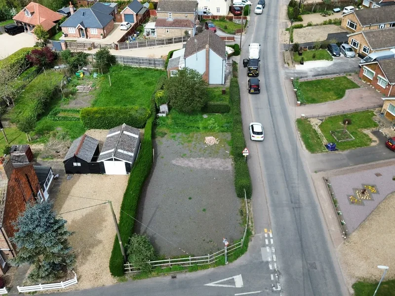 Aerial view of a village road with houses and a vacant plot awaiting development