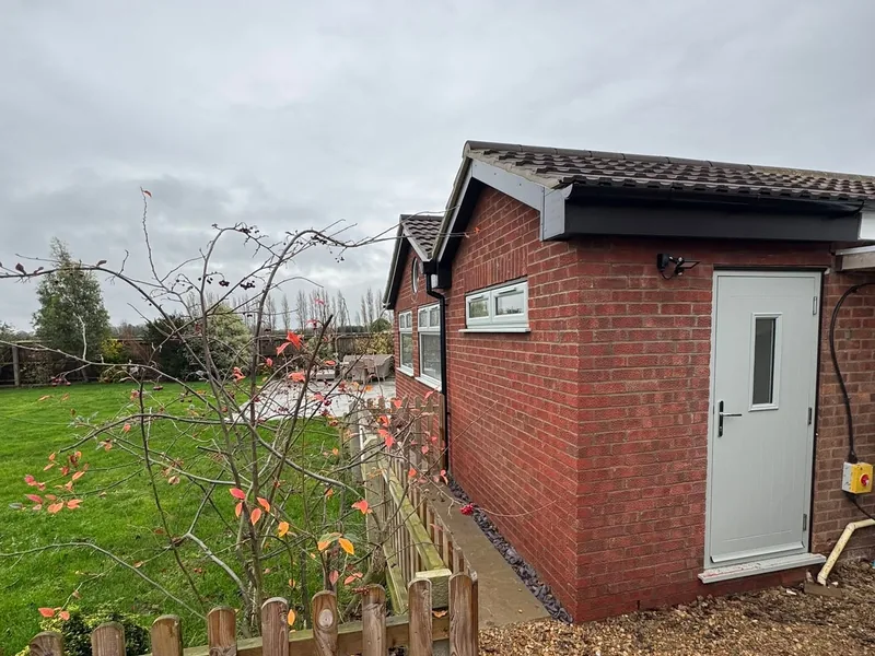 Brick garden room with a tiled roof and white external door beside a lawn