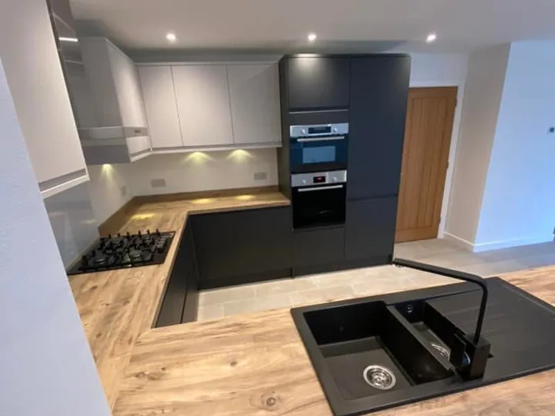 Fitted kitchen with black sink, gas hob and built in ovens beside a new oak door