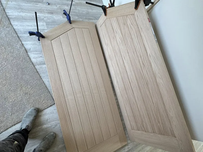 Two light oak panelled doors laid out on the floor being prepared for hanging
