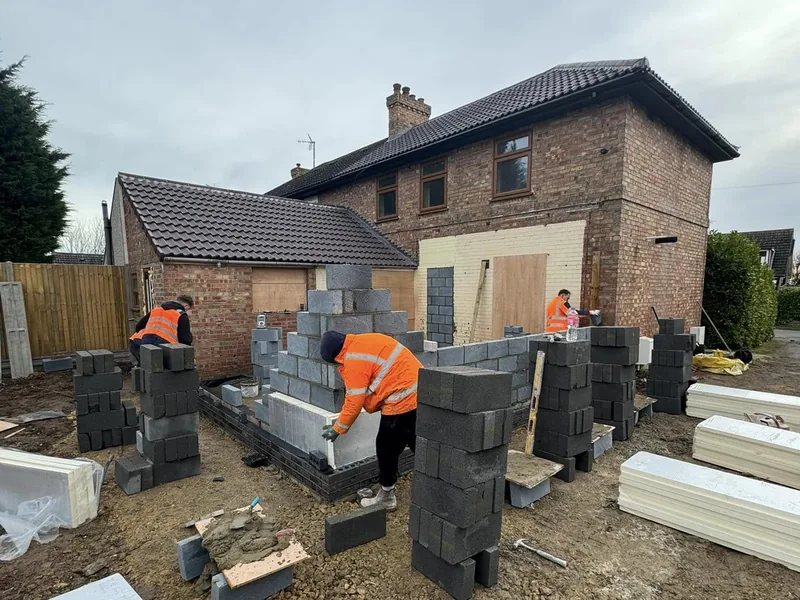 Bricklayers building new blockwork walls for an extension beside a two storey house