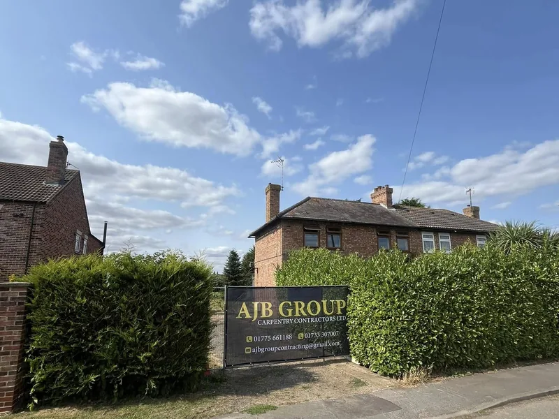 AJB Group site sign board on the boundary hedge outside a brick house