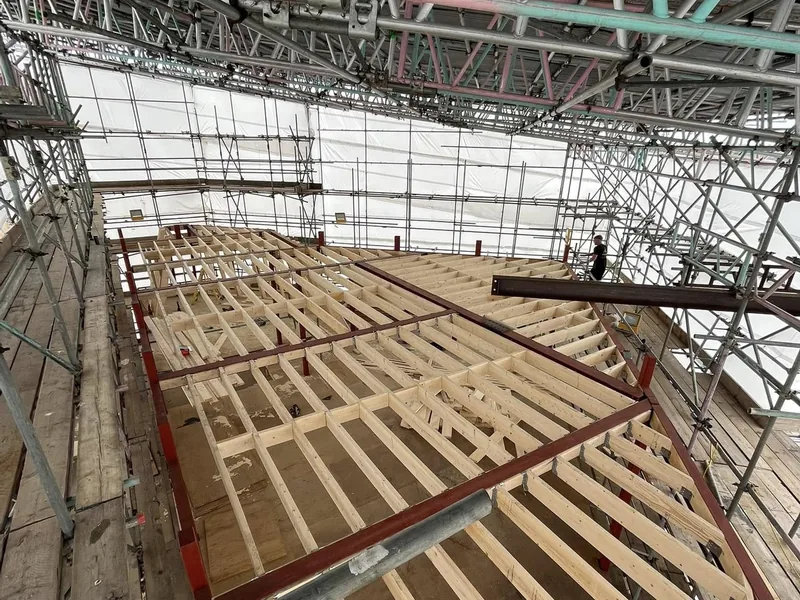 Timber joists installed between steel beams inside a scaffolded shell with a worker on the deck