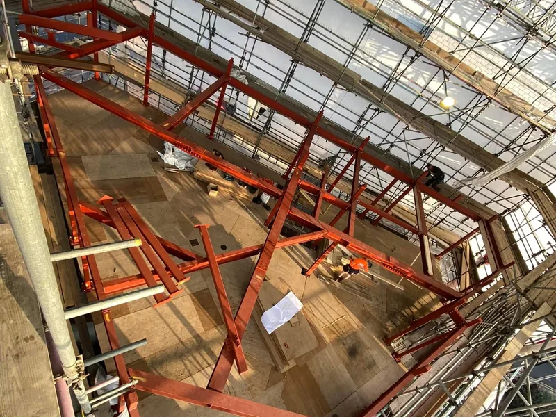 Red painted steel frame inside a scaffolded shell with timber floor deck below