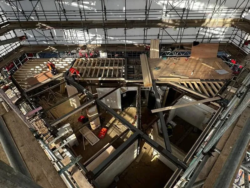 Steel frame, timber stud walls and ply decking at roof level under a temporary scaffold roof