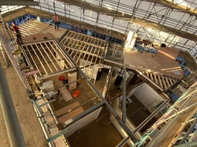 Steel beams and new timber joists at roof level with carpenters working under a scaffold roof