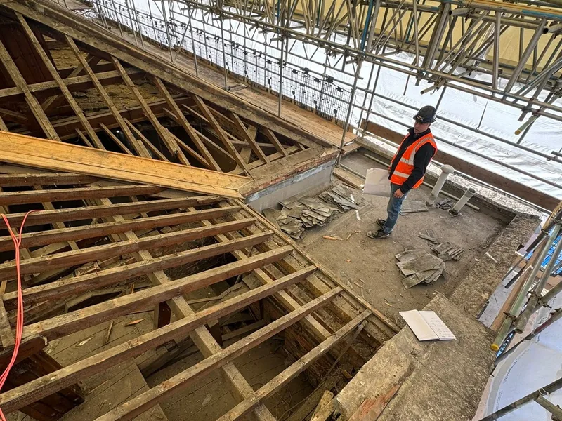 Carpenter on a scaffolded roof stripped back to the existing rafters with a new timber beam fitted