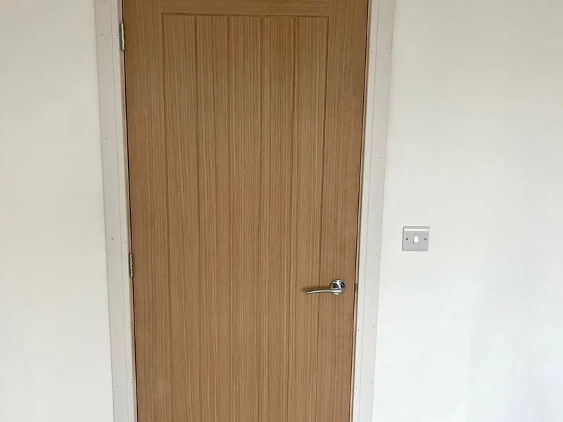 Oak veneer internal door hung in a white painted opening with a chrome lever handle