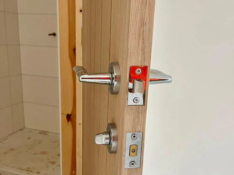 Close up of a chrome lever handle, latch and keep on the edge of an oak internal door