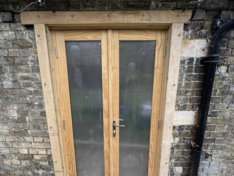 New timber glazed double doors with an oak lintel fitted in a stone and brick wall
