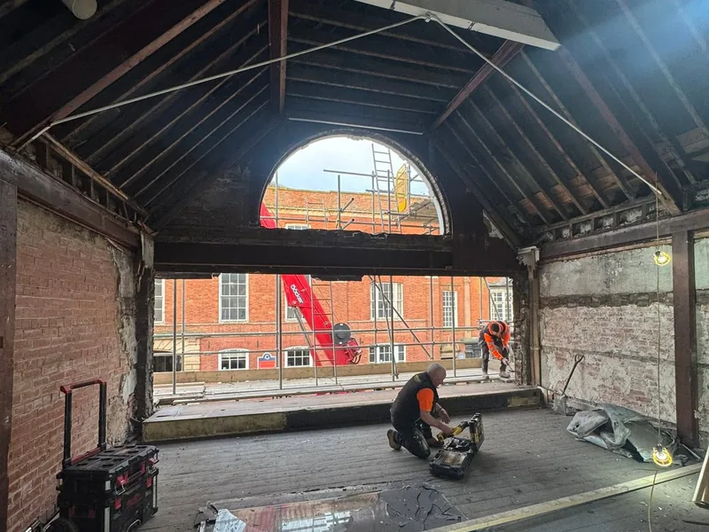 Stripped out interior with exposed roof timbers and a large arched opening, joiner cutting timber