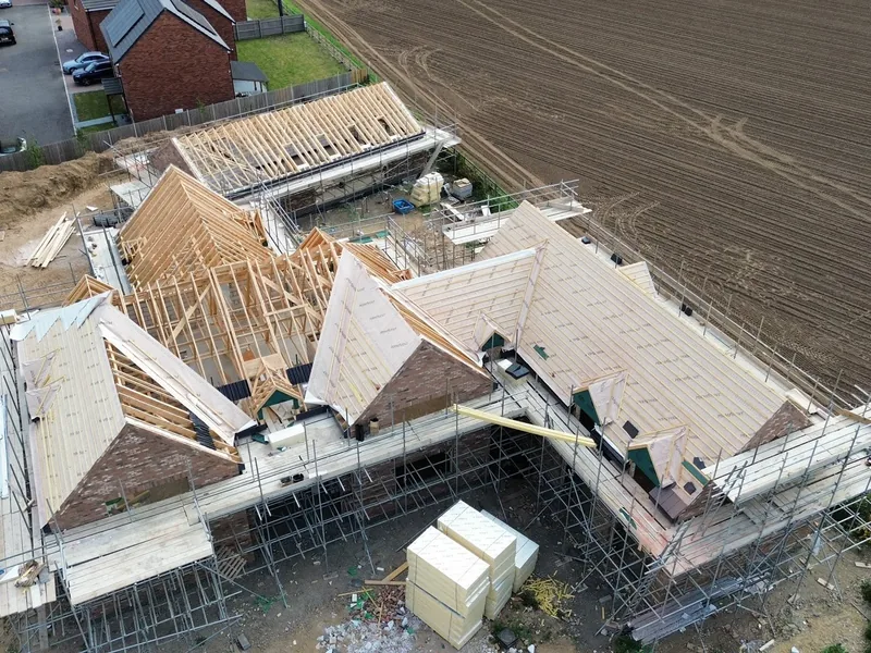 Aerial view of new build houses with roof structures part boarded and scaffolding in place