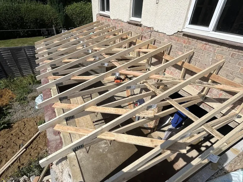 New timber trussed rafters erected over a single storey extension against a rendered house wall