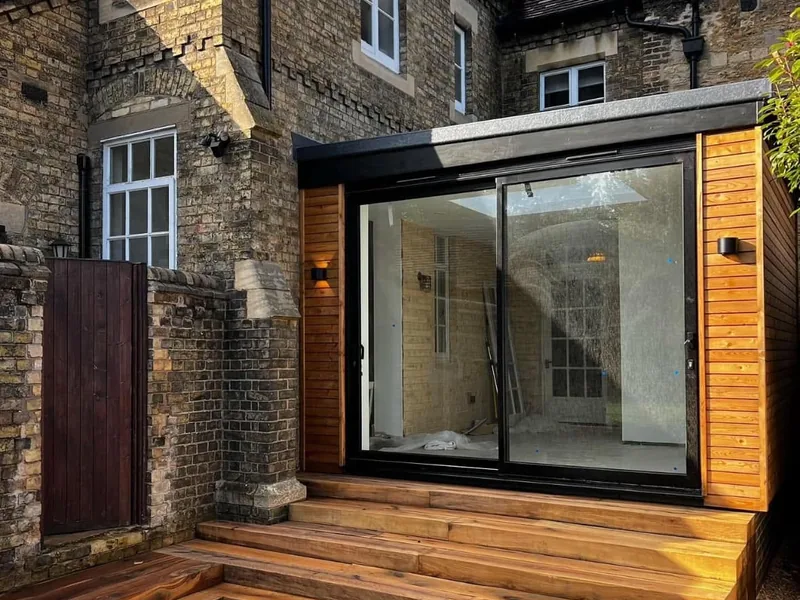 Cedar clad flat roof extension with sliding doors and timber steps on a period brick house