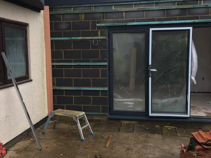 Blockwork extension shell with grey aluminium sliding patio doors fitted and a ladder on the patio