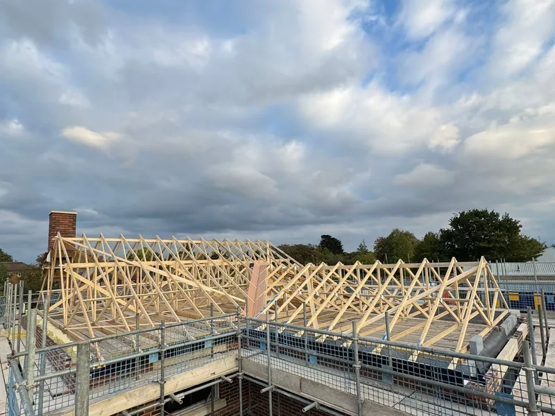 New timber roof trusses erected on a scaffolded building against a cloudy sky