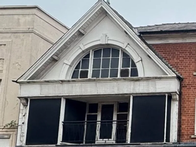 Rendered gable with an arched multi pane window above a first floor doorway and balcony rail