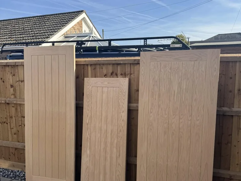 Three unfinished oak veneer cottage style doors standing against a garden fence