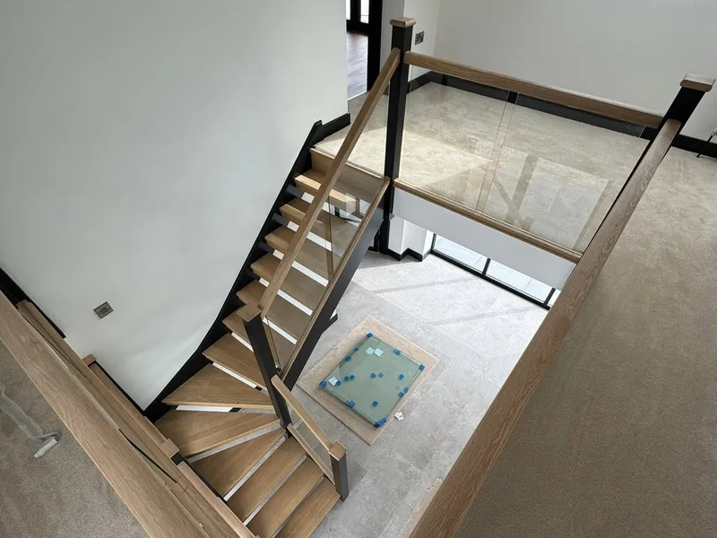 Open riser oak staircase with glass balustrade seen from the landing above