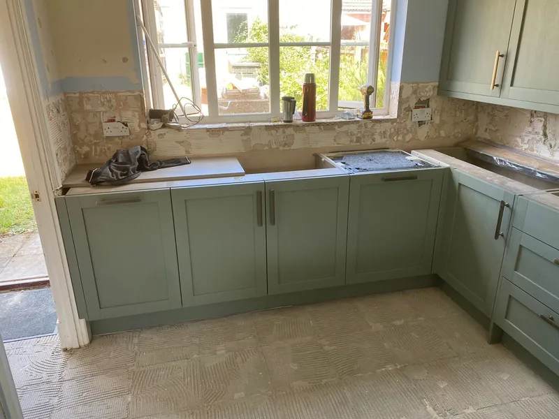 Sage green shaker kitchen units and worktops fitted during a renovation with walls stripped back