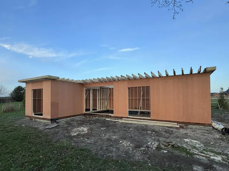 Timber framed single storey lodge with sheathed walls and projecting roof joists in an open field