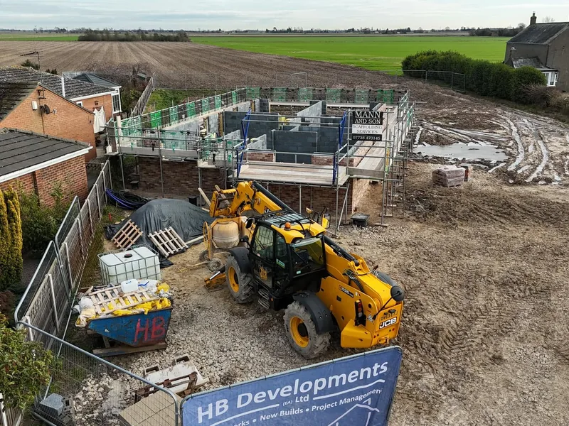 New build plot under construction with scaffolding, a telehandler and materials on a muddy site