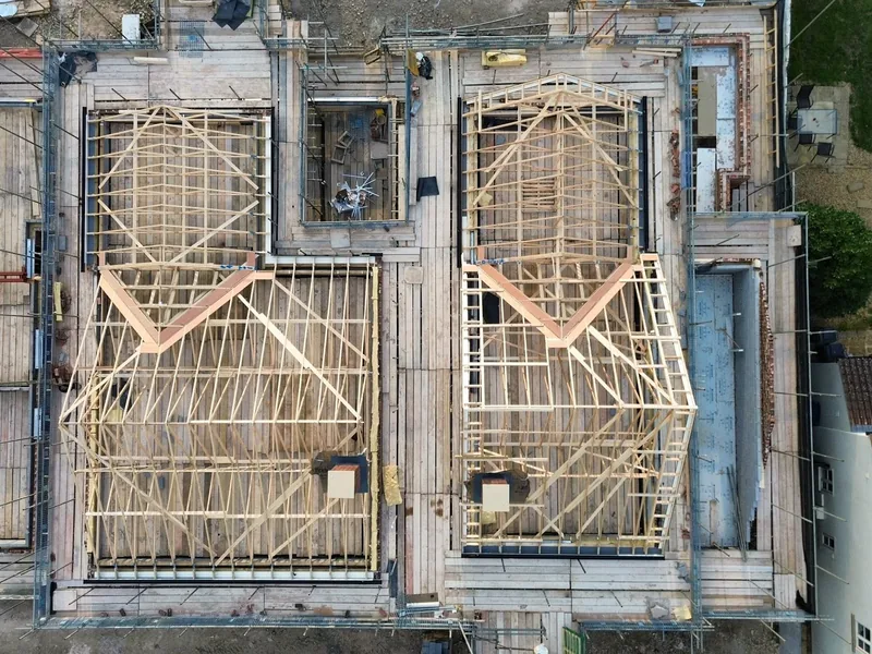 Overhead view of two timber roof structures with hips and valleys framed out on a pair of new builds
