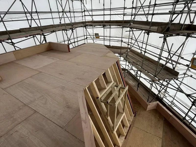 Timber stud framing being built on a plywood deck inside a scaffold and shrink wrap enclosure