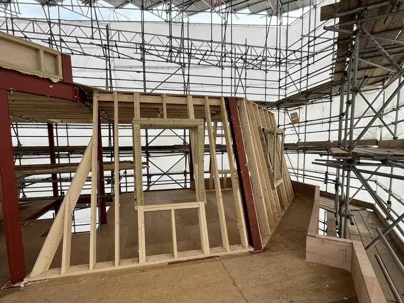 Raking timber stud wall frame erected on a plywood deck beneath scaffolding and a temporary roof