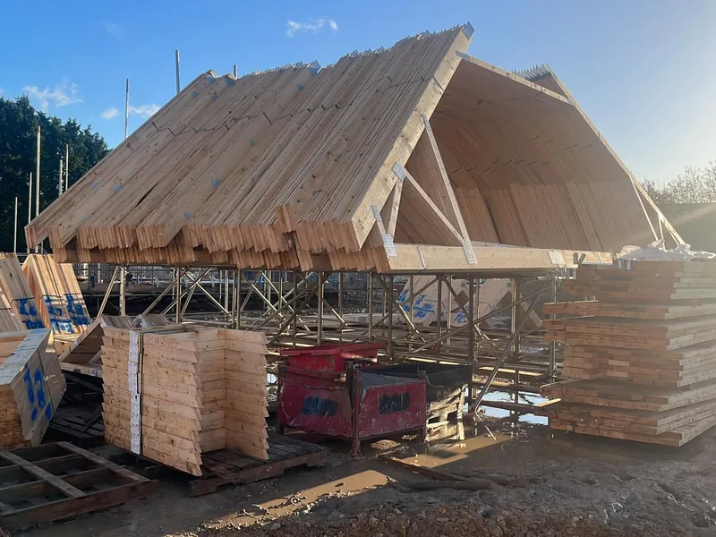 Large steep timber roof structure standing on scaffolding with packs of new timber stacked below