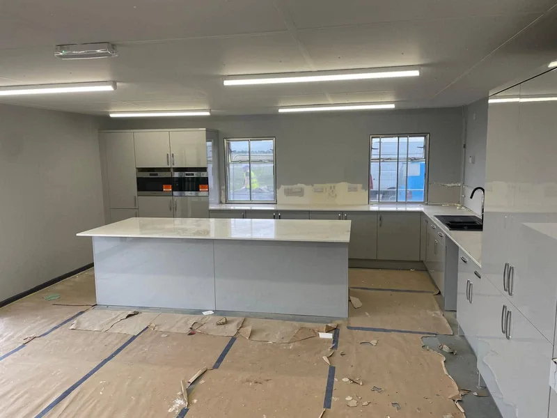 Newly fitted kitchen with island unit and integrated ovens, floor protection still down