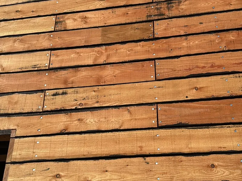 Close up of rough sawn timber cladding boards screw fixed over a black backing
