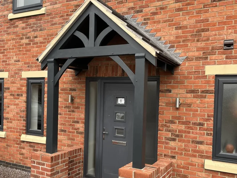 Dark stained timber porch canopy over the front door of a new red brick house