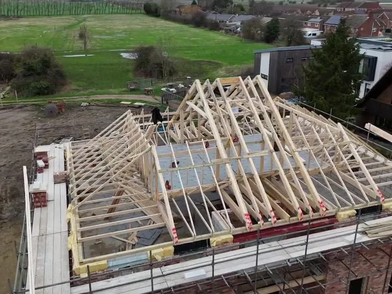 Hipped timber trussed roof structure erected on a new house with scaffolding around it