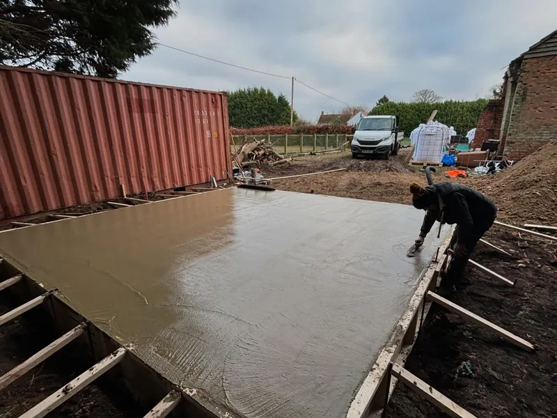Freshly poured concrete slab inside timber shuttering being floated by a worker