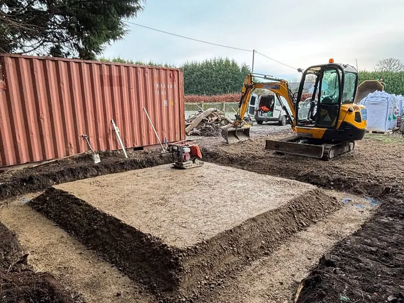 Excavated and compacted sub base pad with a mini digger and compactor plate on site